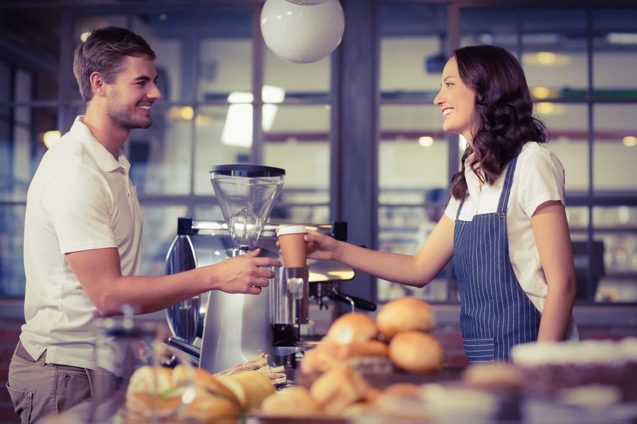 coffee shop worker handing a cup to a customer