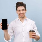 smiling man holding coffee and a phone