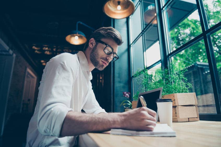 young professional man writing at a coffee shop