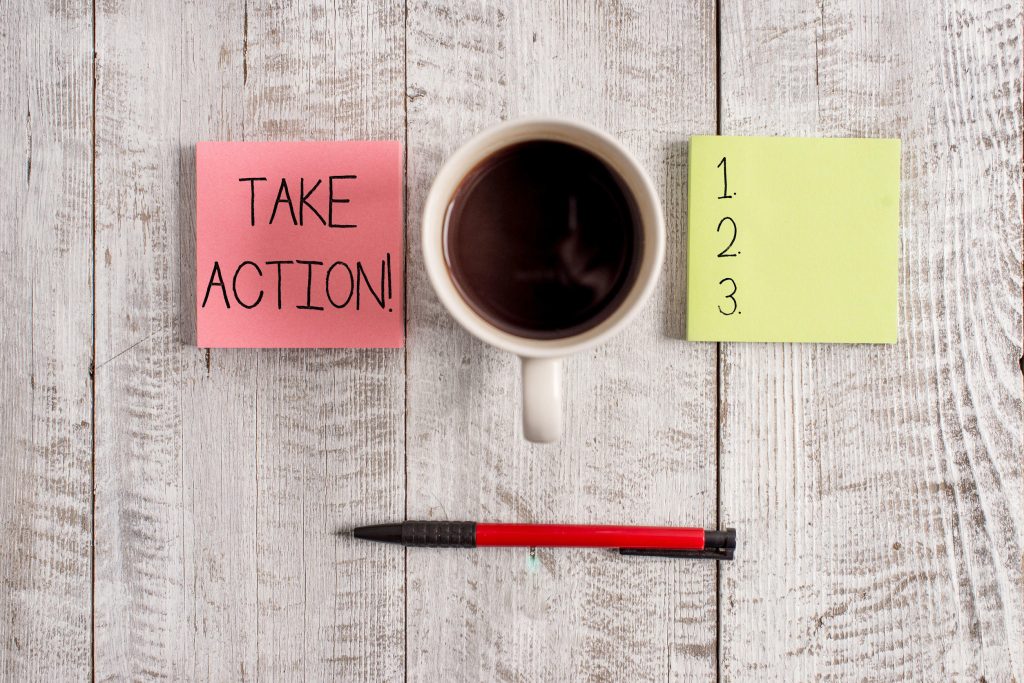 post-it notes showing “take action” and steps 1, 2, and 3; a cup of coffee and a pencil on the table