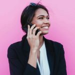 businesswoman smiling while on the phone, standing in front of a pink background