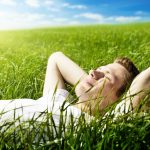 young man closing his eyes and lying in a field of green grass