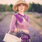 classy woman in a purple dress, standing in a field of lavender, with a basket of flowers