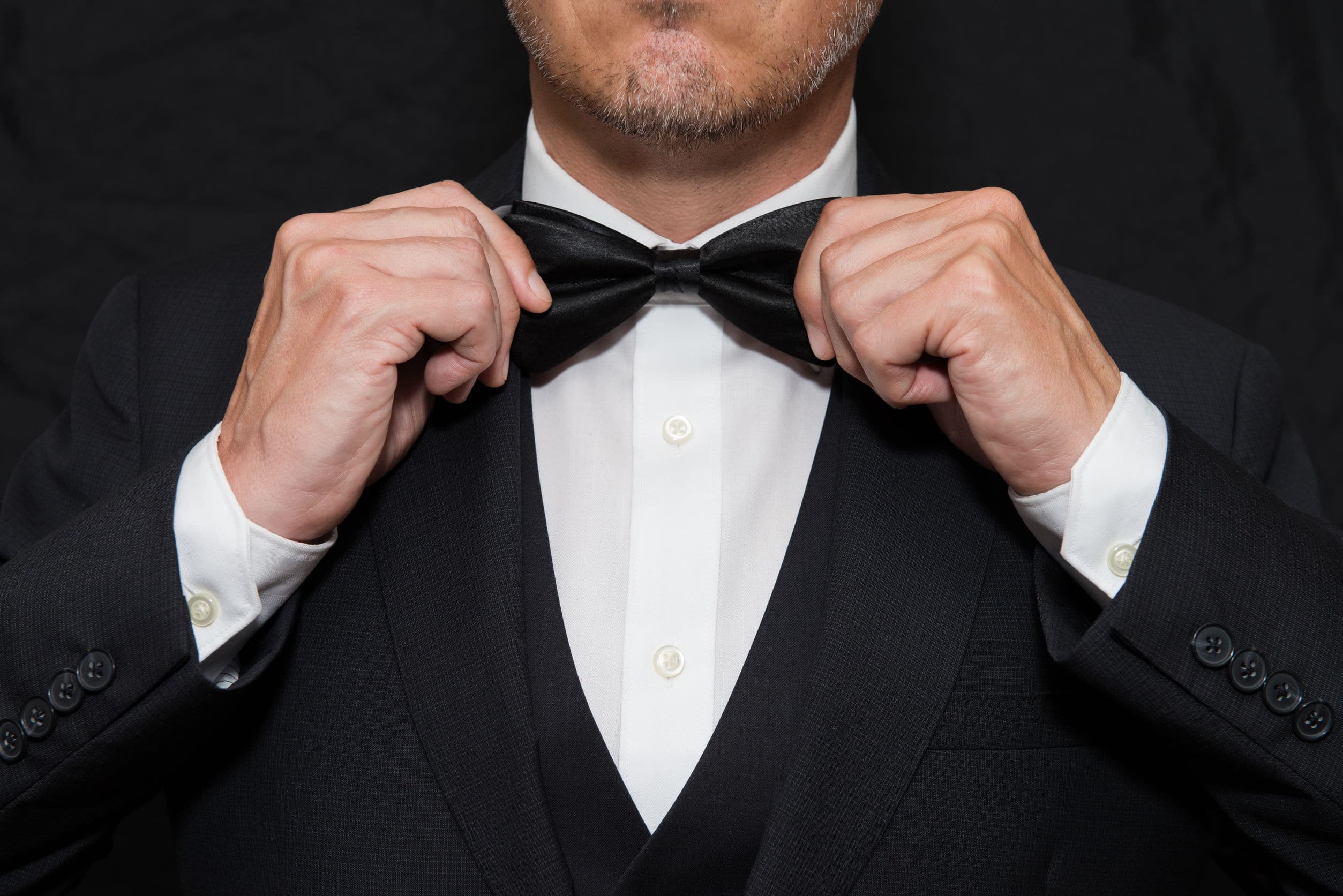 a man in a black tuxedo straightening his black bowtie