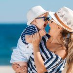 happy seaside mom and baby in matching blue-and-white striped shirts and white hats