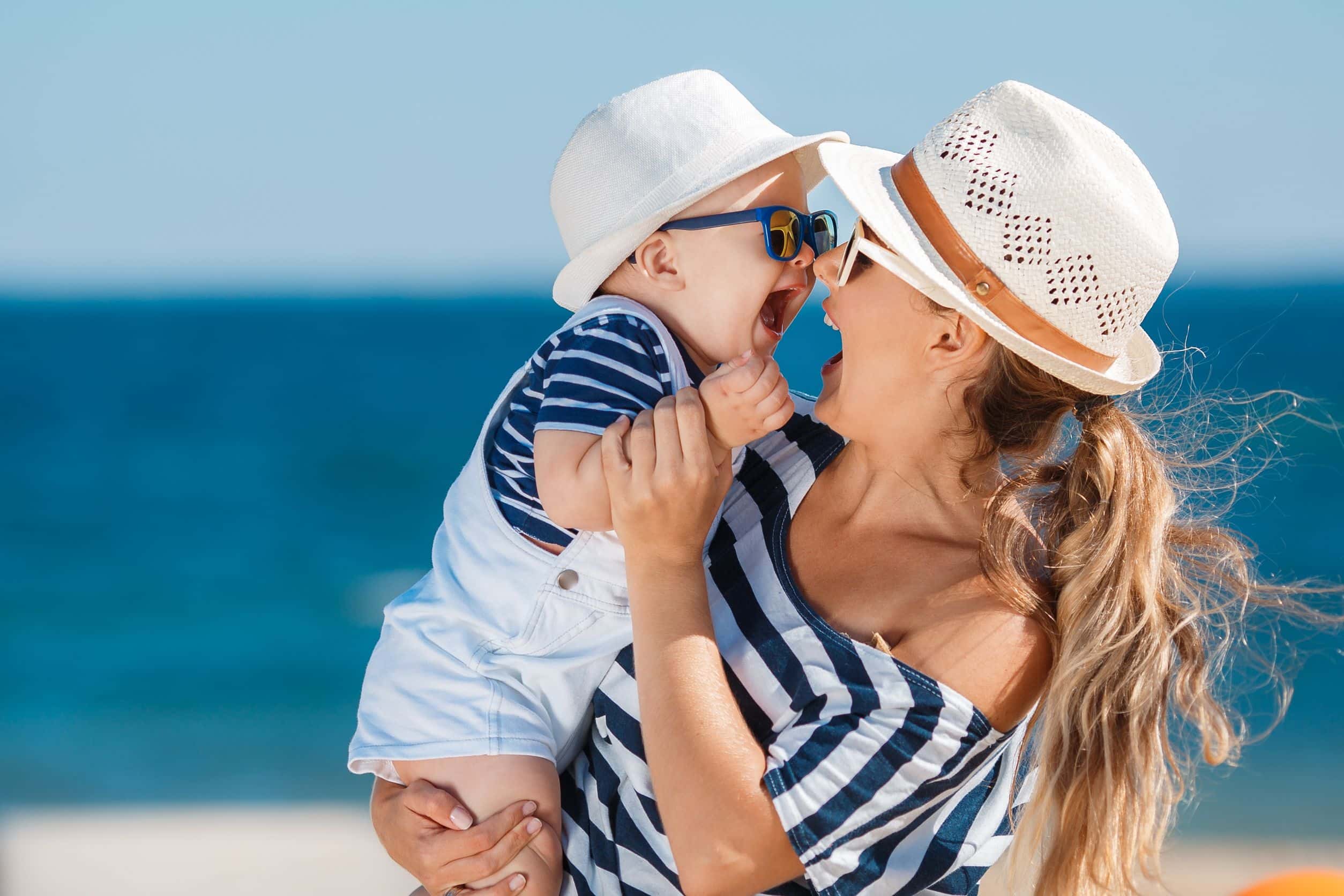 happy seaside mom and baby in matching blue-and-white striped shirts and white hats