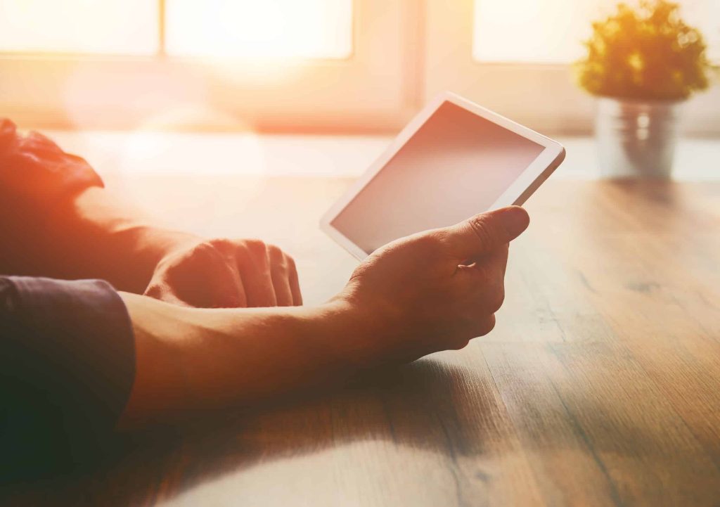 man sitting at his kitchen table in the morning and reading on his tablet