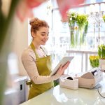 Small business owner checking her tablet, surrounded by flowers in a bright shop