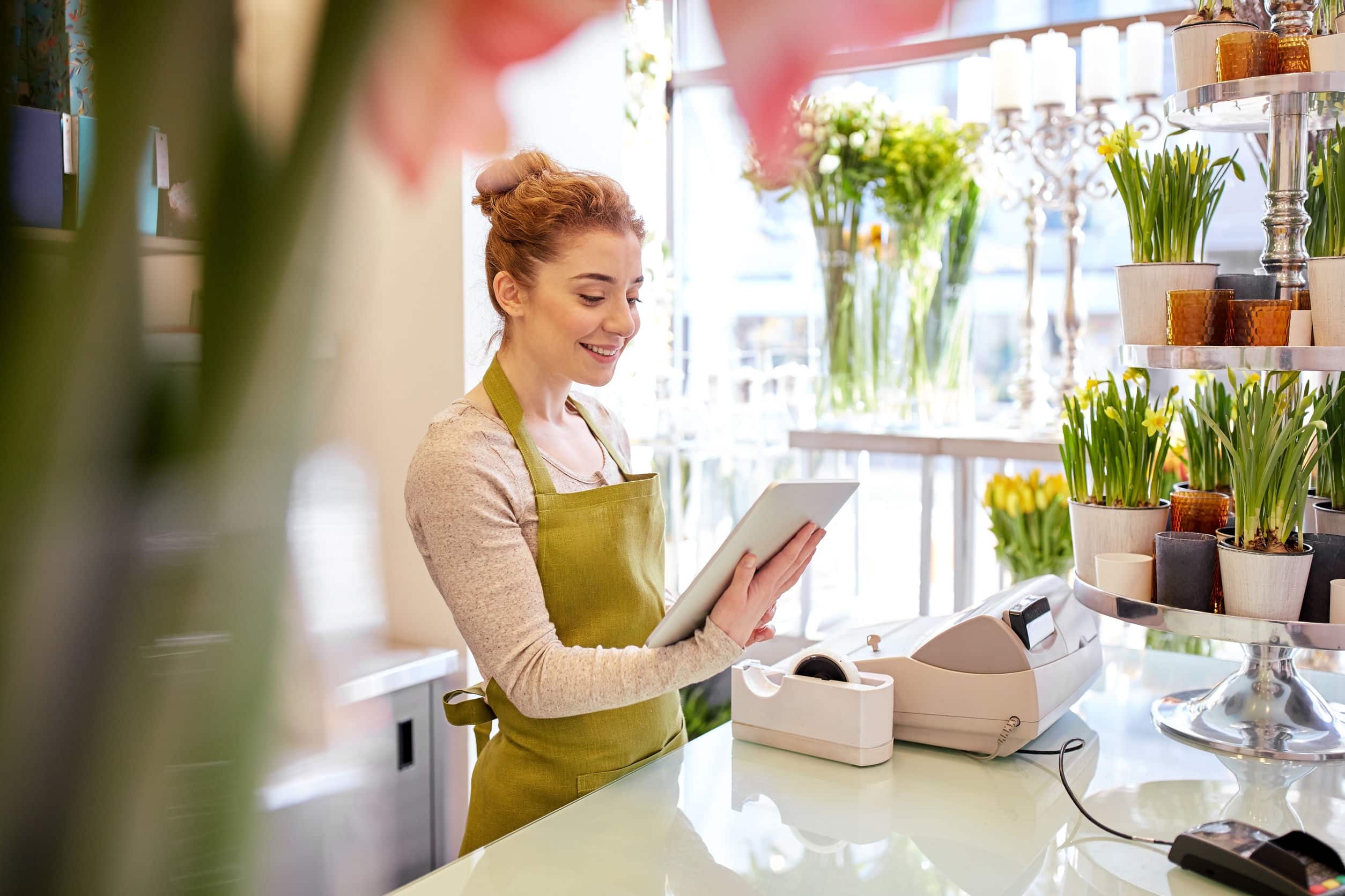 Small business owner checking her tablet, surrounded by flowers in a bright shop