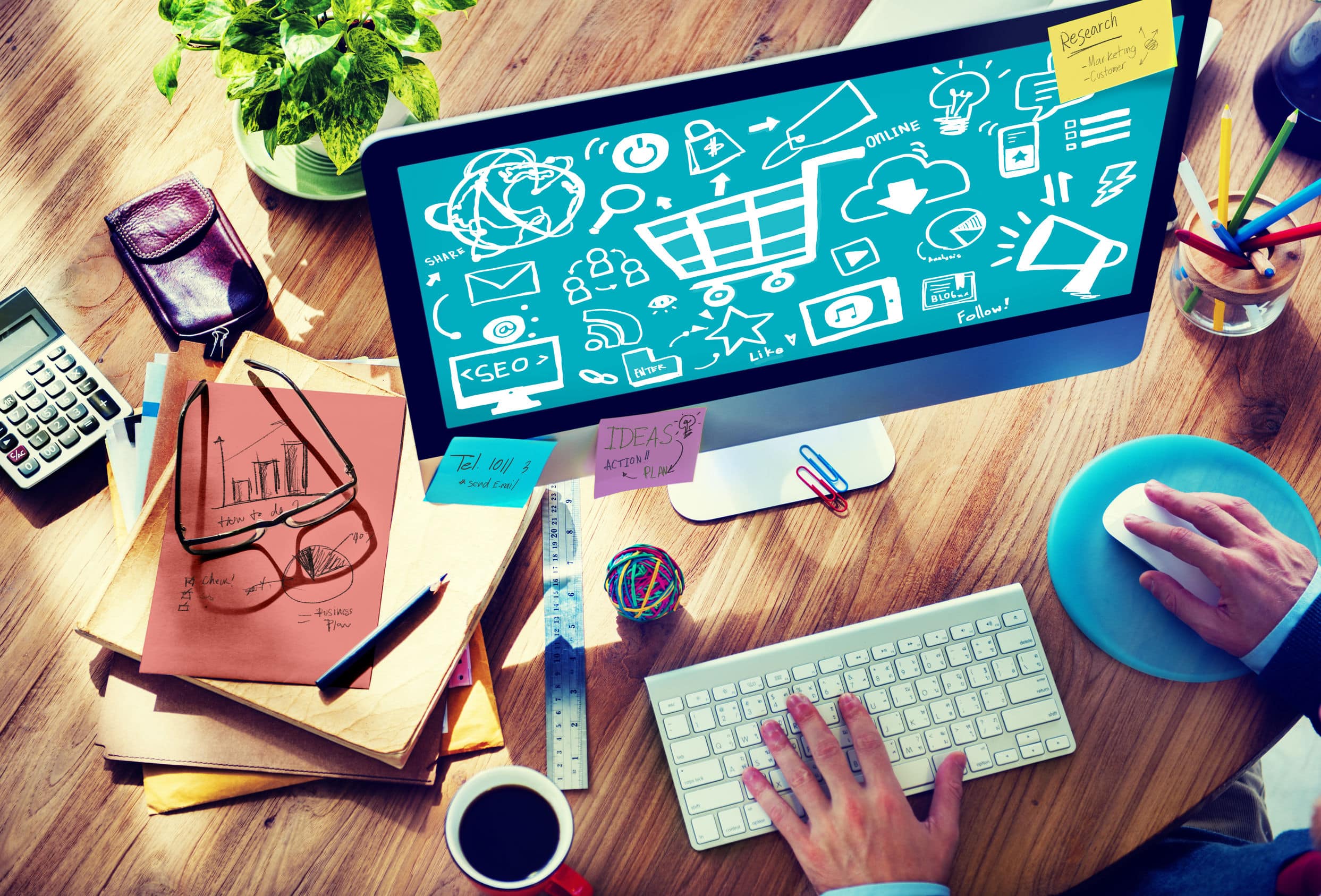 a businessman at his desk with colored pencils, coffee, a plant, and a computer