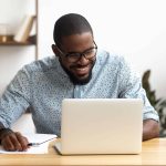 a smiling man on his laptop, planning social media for his small business