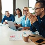 An office worker laughing while sitting with a group of diverse colleagues during a meeting