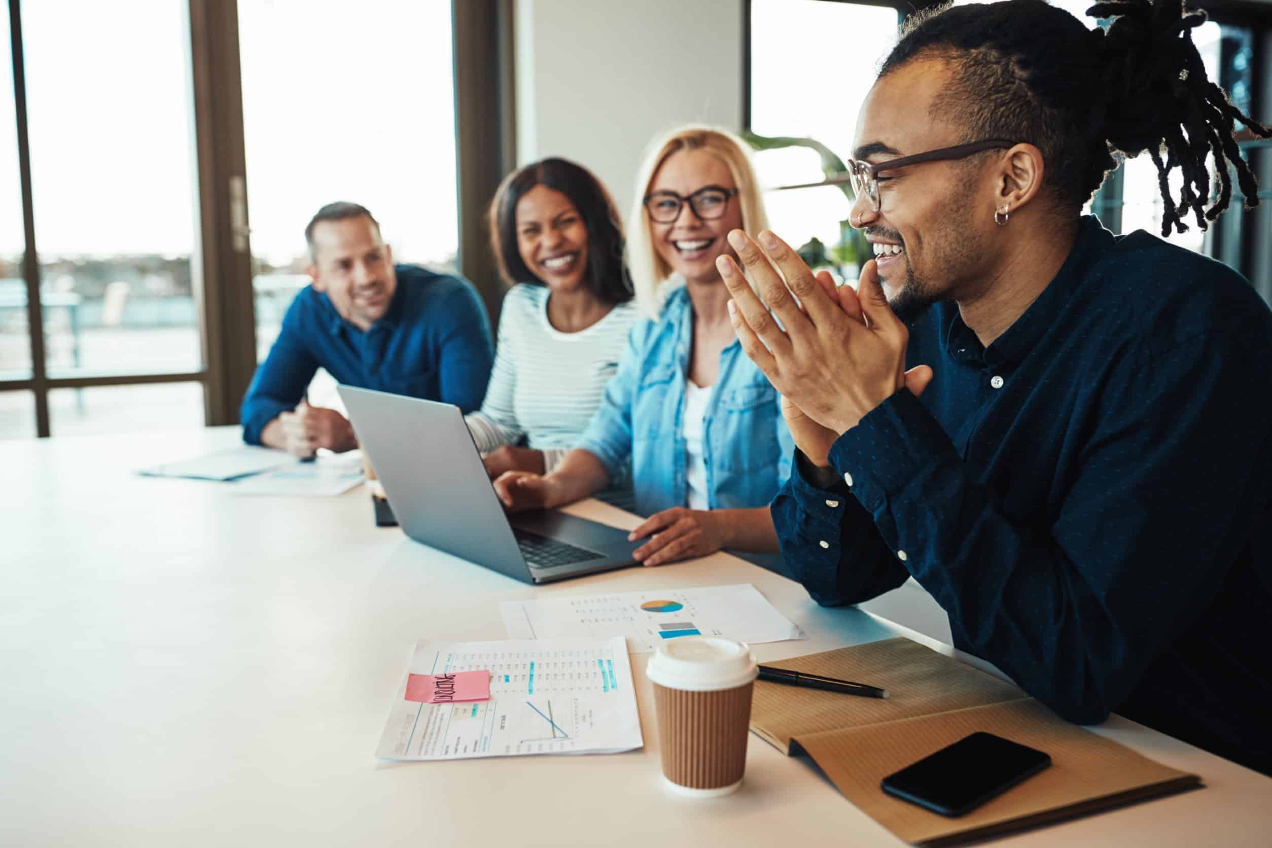 An office worker laughing while sitting with a group of diverse colleagues during a meeting