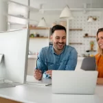 Two coworkers working on a project with a laptop and desktop